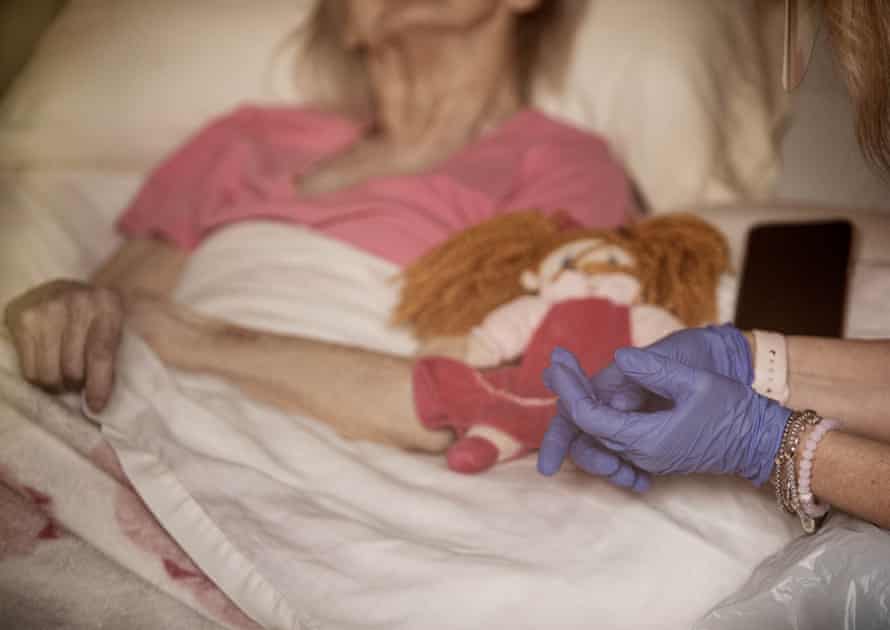 My mom, wearing her PPE, sits next to my grandmother's bed