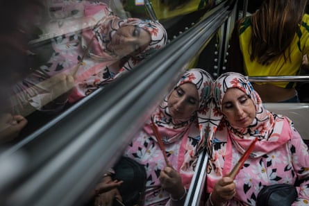 A female passenger wearing a pink scarf with flowers on it, holding a hand fan, is reflected in the window of a Paris Métro train