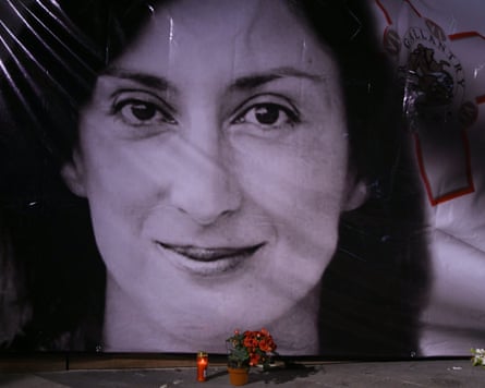 A bunch of flowers and a burning in candle in front of a huge black-and-white portrait of Daphne Caruana Galizia