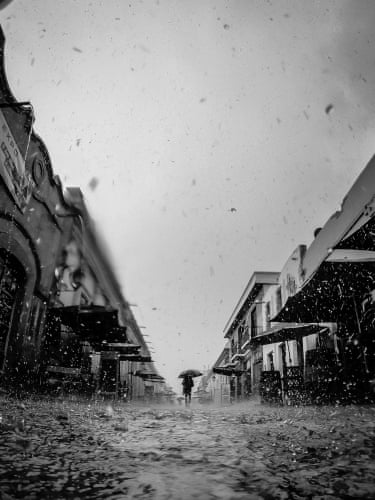 an evocative rainy street scene, a solo figure with an umbrella at the centre of the shot