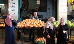 Oranges and watermelons for sale at the market in Bethlehem with three women in headscarfs in front of the stall.