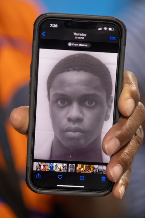 A hand holds an iPhone with a black and white photo of a young man on the screen