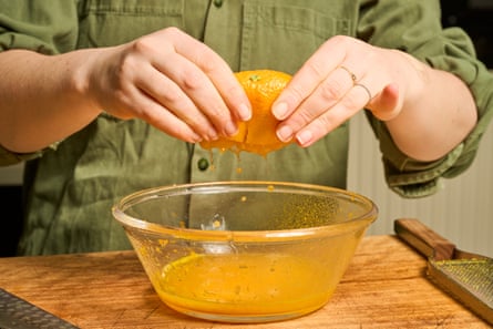 Woman’s hands squeezing orange to get juice into large glass bowl