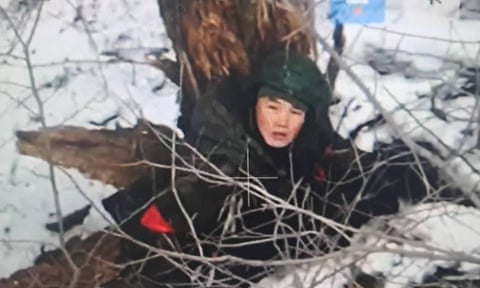 Person crouched down in snow next to damaged tree trunk