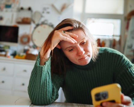 Middle-aged female upset, looking astatine her smartphone surface astatine home