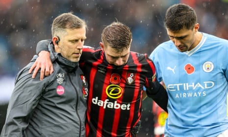 A stricken Alex Scott is helped from the field by a Bournemouth physio and Manchester City midfielder Rodri.