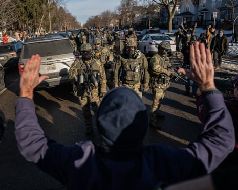 A person holds their hands aloft in front of federal enforcement officers