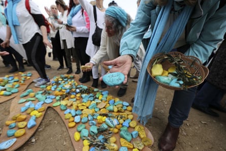 Women wearing blue scarves place blue and yellow pebbles on to a wooden template.