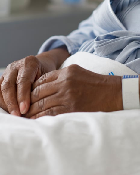 close up of a Black woman's clasped hands while recovering in a hospital bed