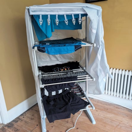 A heated clothes airer with a cover holds drying laundry near a radiator