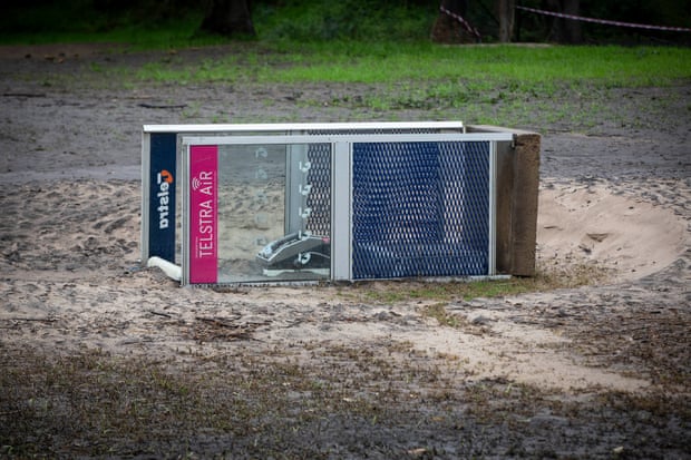 A Telstra phone booth on its side in mud