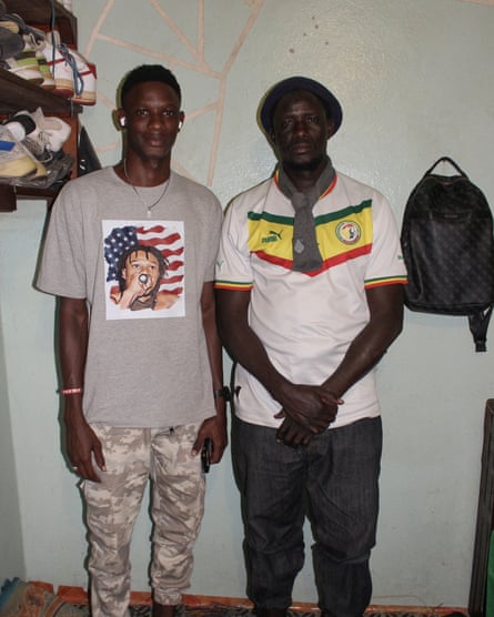 Two young black men stand by a wall as they pose for a photo