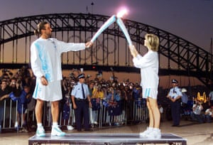 Olivia Newton-John passes the Olympic flame to tennis player Patrick Rafter in front of Sydney Harbour Bridge.