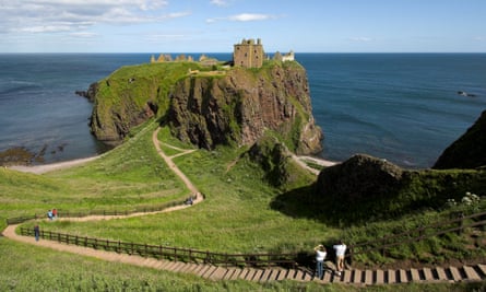A view of Dunnottar castle, the path through grassland leading to it and the sea beyond