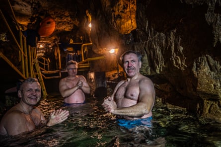 Three men stand in cold water wearing swimming shorts