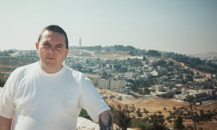 A man in a white T-shirt looks at the camera with