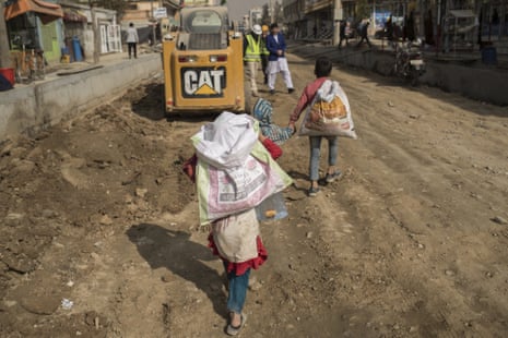 Two small children carrying sacks seen from behind as they walk along