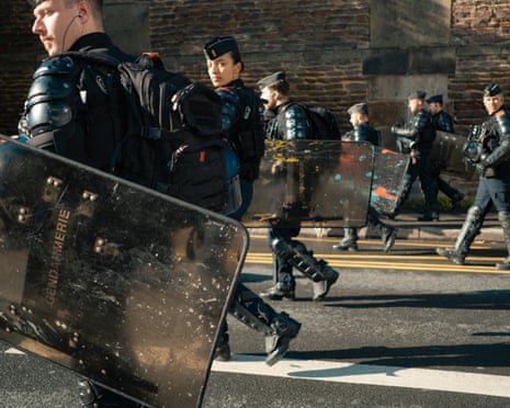 Riot police carrying shields marked "Gendarmerie" escort a protest march through Rennes