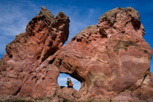 A cellist plays in a gap in a red rock formation under a blue sky