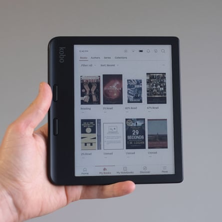 A hand holds a Kobo Libra Colour e-reader in front of a grey wall.