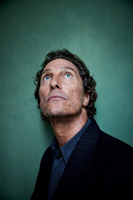 A portrait of Matthew McConaughey against a green background, looking upwards in a dark shirt and jacket