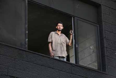 Man stands looking from his window in burnt-out home.