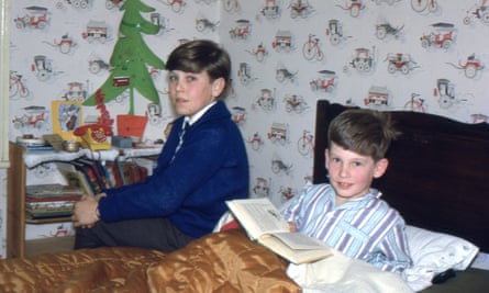 Two boys, one lying in bed with a book and the other sitting on it.