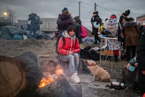 A woman and her dog sit by a fire to keep warm
