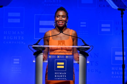 a woman wearing orange dress speaks at a podium
