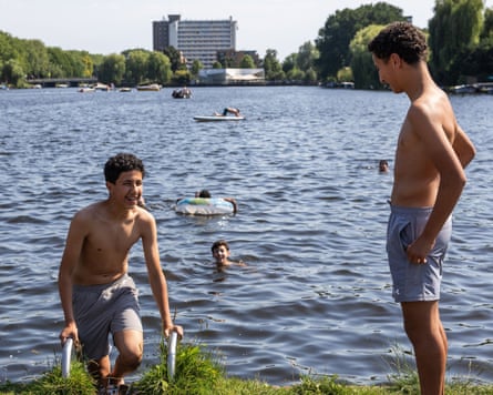 Two men by a large expanse of water with some people swimming in it.