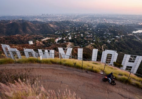 A cyclist rides along a hillside path above the Hollywood sign at dusk