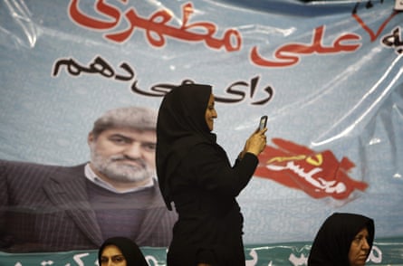 A woman snaps pictures with her mobile phone in front of a campaign poster that rads ‘I will vote for Ali Motahari’.