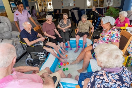 Activities Coordinator Melissa (right) dips her feet in a cold paddling pool with residents at the Red Rose Care Home in Ebbw Vale, South Wales, UK.