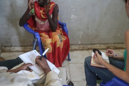 A woman in a brightly coloured dress speaks while two people sit opposite taking notes.