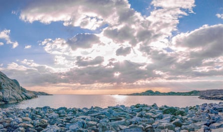 Late afternoon sun breaking through clouds on to a calm sea with rocky foreshore
