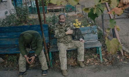 Oleksandr Isaiev in fatigues strokes a tabby cat while sitting on a bench next to a military colleague