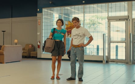 A man and a woman in a big empty room. The woman is wearing a short skirt and a blue top. The man is wearing jeans and a white T-shirt.