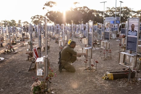 An Israeli soldier crouches to light a candle at a memorial with pictures of victims.