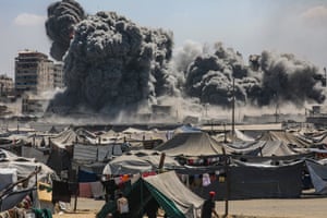 Tents in the foreground and plumes of black smoke and dust in the distance