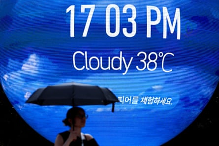 A person carrying an umbrella walks past a spherical digital display showing 38 degrees Celsius during a severe heatwave warning in Seoul on 7 August 2026.