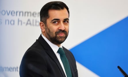 Humza Yousaf, in a suit, shirt and tie, with a slight beard, looks behind him with a slightly bemused expression