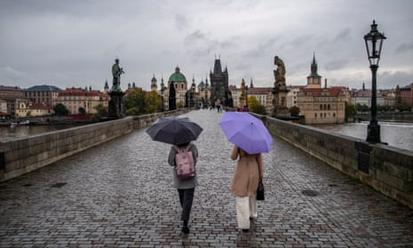 Women covered by umbrellas walk on an almost abandoned Charles Bridge in Prague, Czech Republic