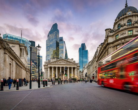 Sunset view of the City of London, England, with commuter and street traffic in front of the Bank of England.