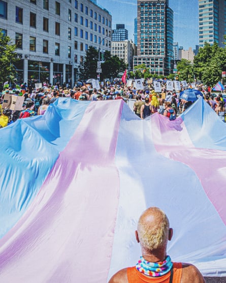 People in a big crowd hold a massive pink, blue and white transgender flag