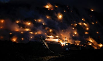 An excavator operator tries to contain the fire as smoke rises from burning rubbish