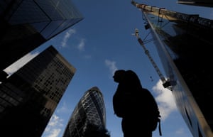 A worker walks past office skyscrapers in the City of London financial district