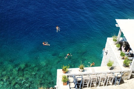 Four people swimming in dark blue sea off a white hotel
