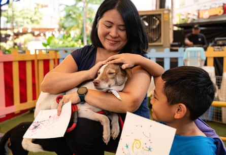 Basti sits with his eyes closed on a woman’s lap who pets his head along with a boy sitting beside them