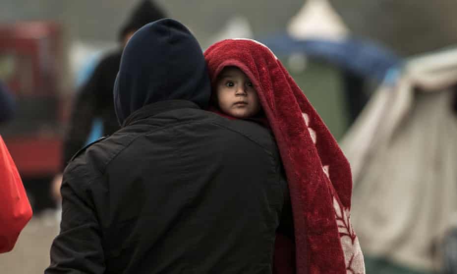 A migrant carries a child in a camp near Dunkirk