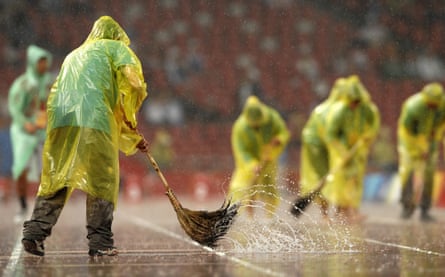A worker sweeps the track at the National Stadium during heavy rain